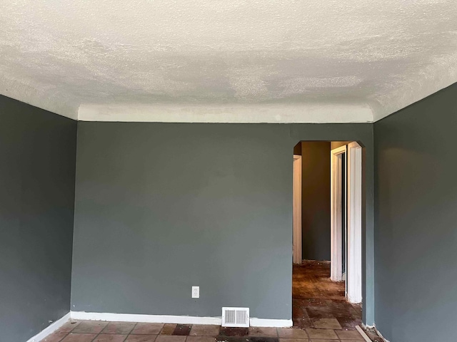 unfurnished room with arched walkways, a textured ceiling, visible vents, and baseboards