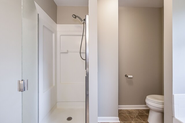 bathroom featuring baseboards, tile patterned floors, a stall shower, and toilet