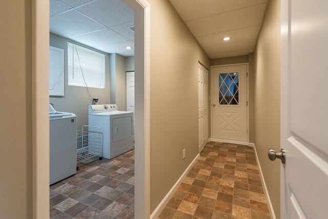 hallway with washer and dryer, baseboards, stone finish flooring, and a paneled ceiling