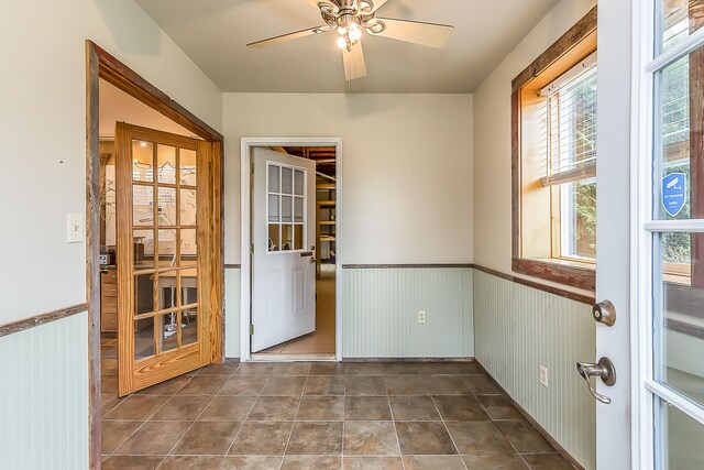 interior space with dark tile patterned flooring, a wainscoted wall, and ceiling fan