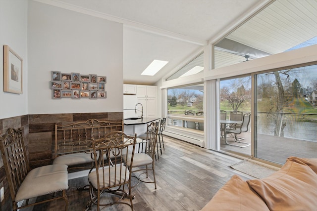 dining space featuring lofted ceiling with skylight, crown molding, light wood-style floors, and a baseboard heating unit