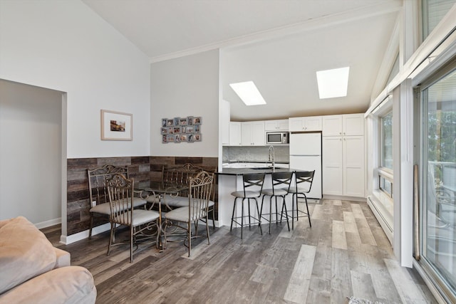 dining room with high vaulted ceiling, light wood-style floors, a skylight, and a baseboard radiator