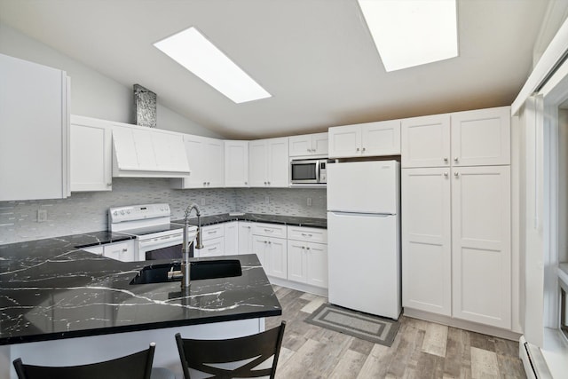 kitchen with a peninsula, a baseboard radiator, white appliances, vaulted ceiling with skylight, and white cabinetry