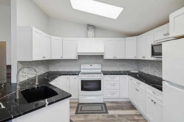 kitchen with white appliances, vaulted ceiling, white cabinets, and a sink