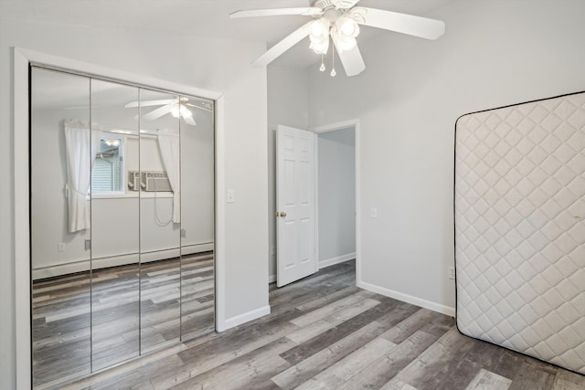 unfurnished bedroom with a closet, a baseboard radiator, baseboards, wood finished floors, and a ceiling fan