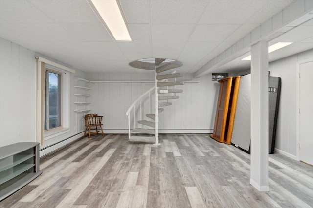 below grade area featuring baseboards, stairs, wood finished floors, and a drop ceiling