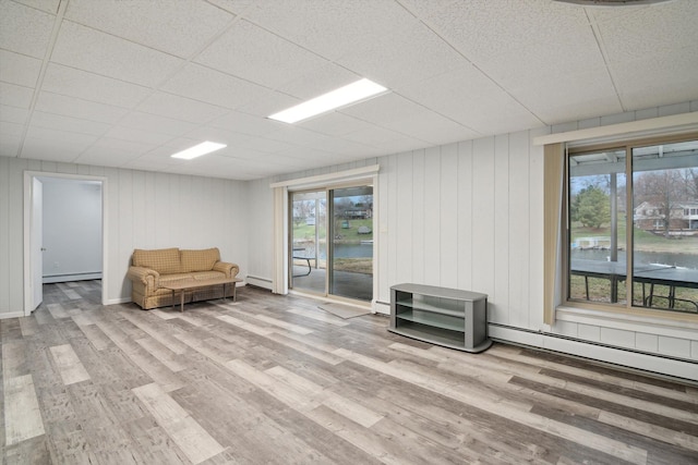 unfurnished room with wood finished floors, a drop ceiling, baseboard heating, and a baseboard radiator