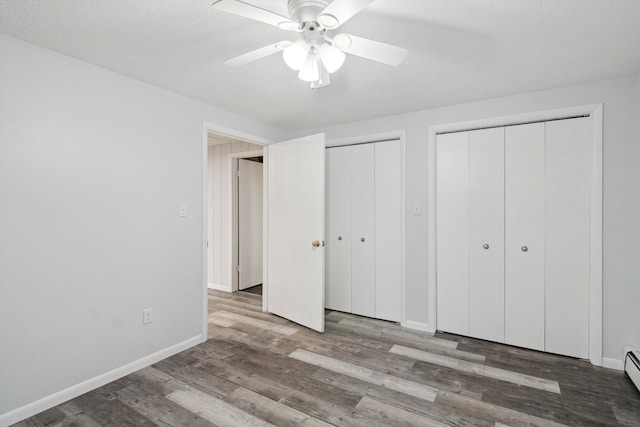 unfurnished bedroom featuring baseboards, baseboard heating, wood finished floors, and two closets