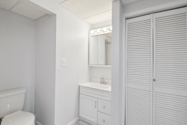 bathroom with baseboards, toilet, a paneled ceiling, and vanity