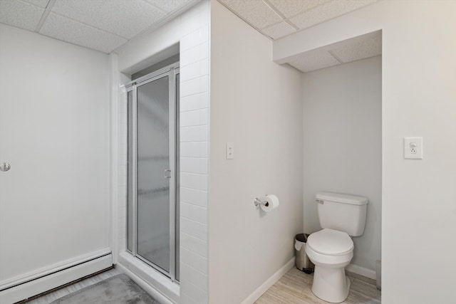 full bathroom with baseboards, toilet, a baseboard heating unit, a stall shower, and a paneled ceiling