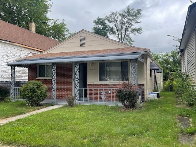 bungalow featuring a front yard, brick siding, a porch, and a shingled roof