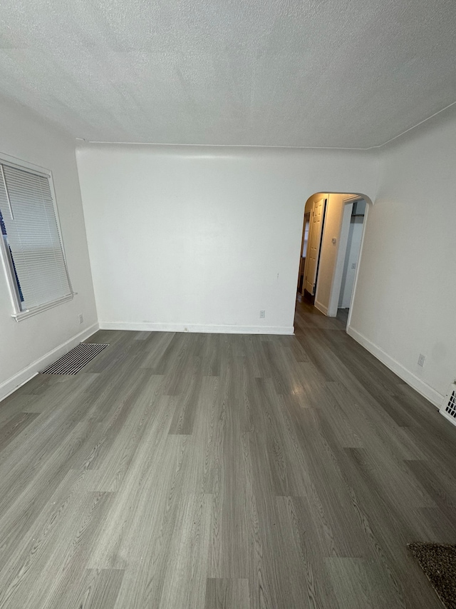 unfurnished living room featuring visible vents, baseboards, arched walkways, dark wood-style floors, and a textured ceiling