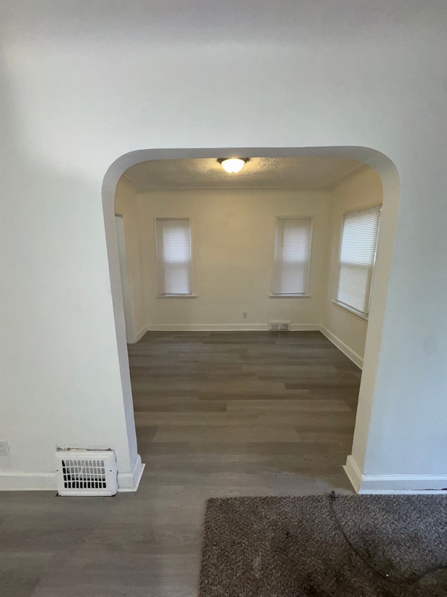 empty room with visible vents, baseboards, arched walkways, and wood finished floors