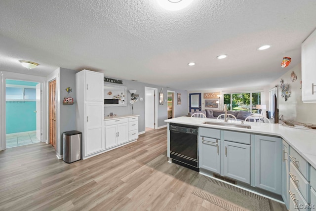 kitchen featuring a sink, light wood-style floors, dishwasher, a textured ceiling, and a peninsula