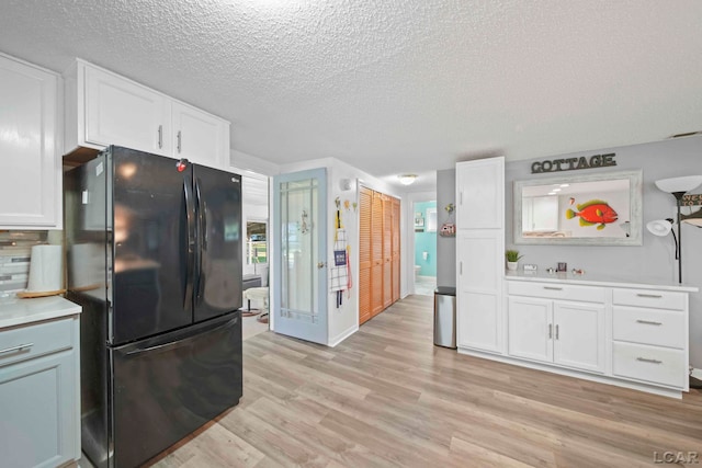 kitchen with white cabinets, light countertops, a textured ceiling, freestanding refrigerator, and light wood-type flooring