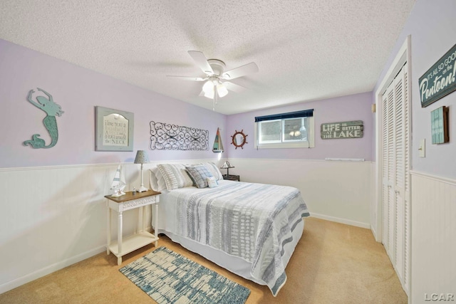 carpeted bedroom with a wainscoted wall, a ceiling fan, a closet, and a textured ceiling