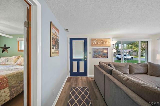 living area with dark wood-type flooring, a textured ceiling, baseboards, and visible vents