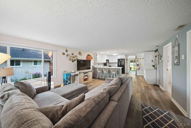 living room featuring a textured ceiling, visible vents, wood finished floors, baseboards, and recessed lighting