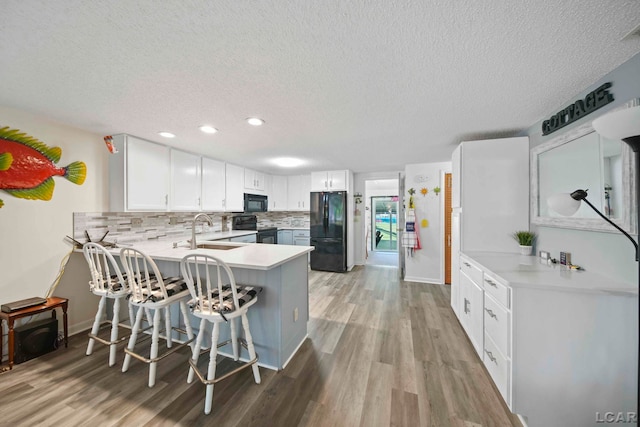 kitchen featuring a textured ceiling, light wood-type flooring, a sink, black appliances, and a peninsula