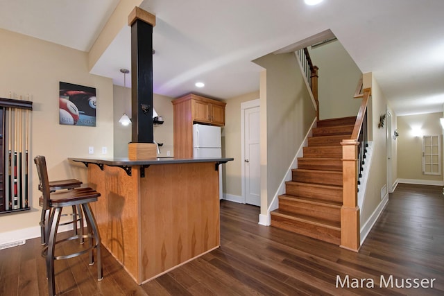 8821 Summerset Woods Ct SE, Alto, MI 49302 - kitchen with freestanding refrigerator, a kitchen breakfast bar, dark wood-style flooring, a peninsula, and dark countertops