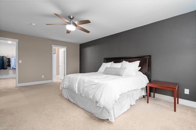 bedroom with a spacious closet, baseboards, light colored carpet, and ceiling fan