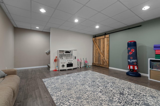 playroom featuring a drop ceiling, baseboards, a barn door, and wood finished floors