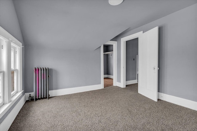 carpeted empty room featuring radiator, baseboards, and vaulted ceiling