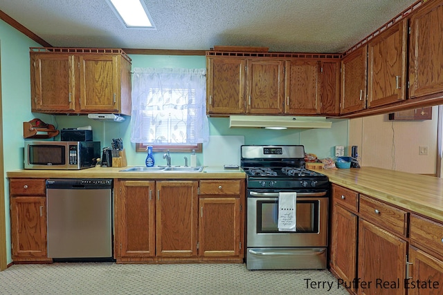 kitchen featuring light countertops, stainless steel appliances, under cabinet range hood, a sink, and brown cabinetry