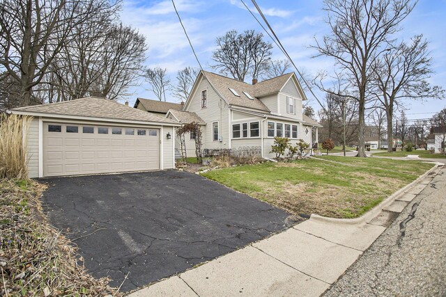 view of front facade featuring a shingled roof, a detached garage, and a front yard