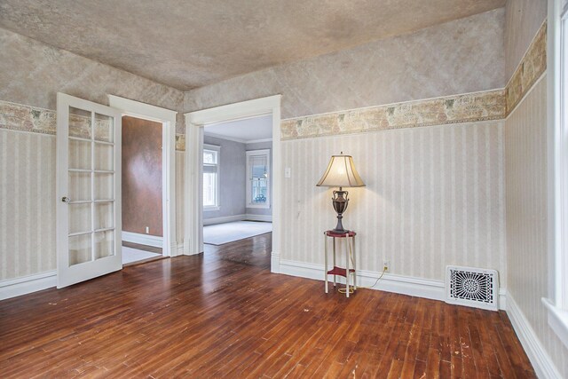 spare room with hardwood / wood-style floors, wallpapered walls, baseboards, and visible vents