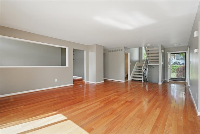 unfurnished living room featuring stairway, light wood finished floors, and baseboards