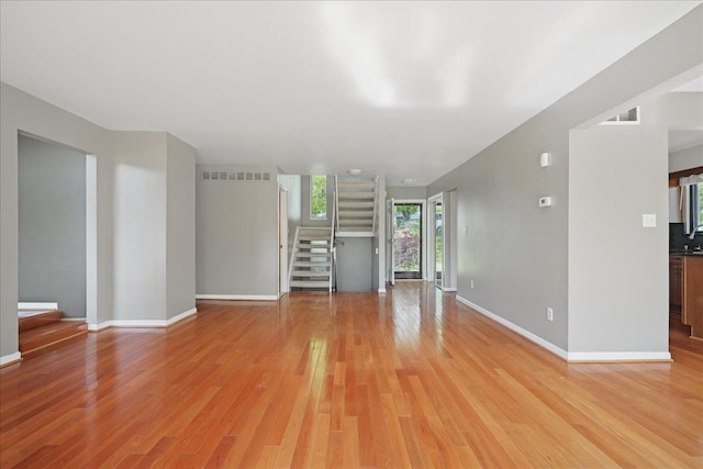unfurnished living room with stairway, light wood finished floors, and baseboards