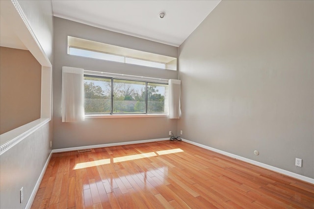 unfurnished room featuring light wood finished floors, baseboards, and vaulted ceiling