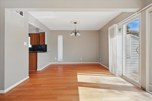 unfurnished dining area featuring a chandelier, light wood finished floors, and baseboards