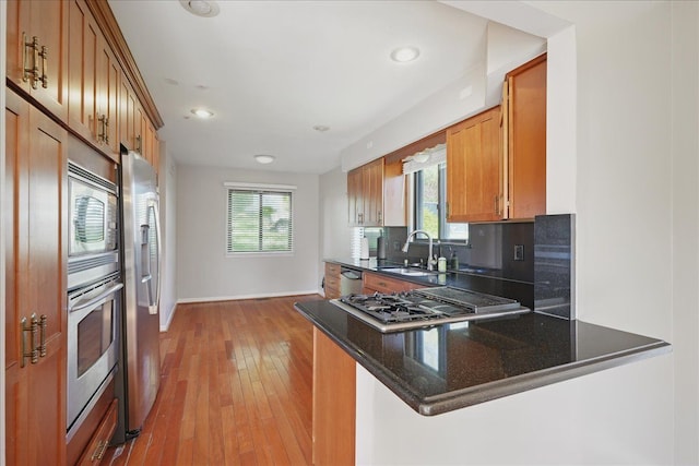 kitchen with appliances with stainless steel finishes, a sink, a peninsula, baseboards, and backsplash