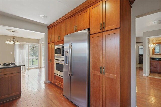 kitchen with appliances with stainless steel finishes, brown cabinetry, light wood-style flooring, and a chandelier