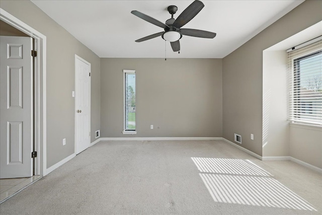 empty room featuring healthy amount of natural light, a ceiling fan, light carpet, and baseboards