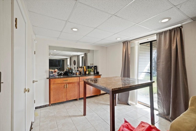 kitchen with brown cabinetry, a paneled ceiling, dark countertops, recessed lighting, and light tile patterned flooring