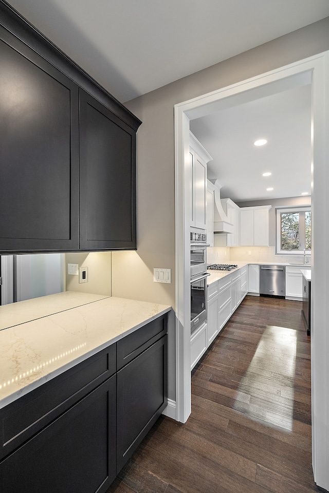kitchen featuring light stone countertops, appliances with stainless steel finishes, custom range hood, white cabinets, and dark wood-type flooring