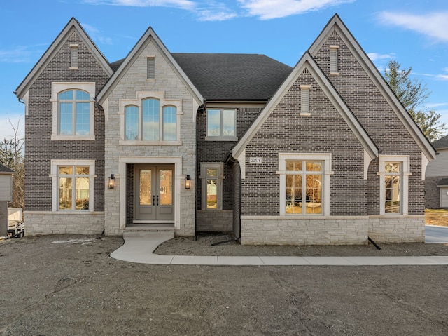 french country style house featuring french doors, stone siding, brick siding, and a shingled roof