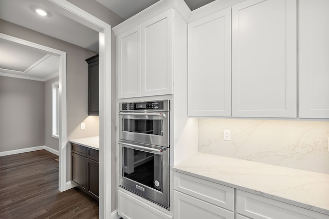 kitchen featuring tasteful backsplash, stainless steel double oven, dark wood finished floors, baseboards, and ornamental molding