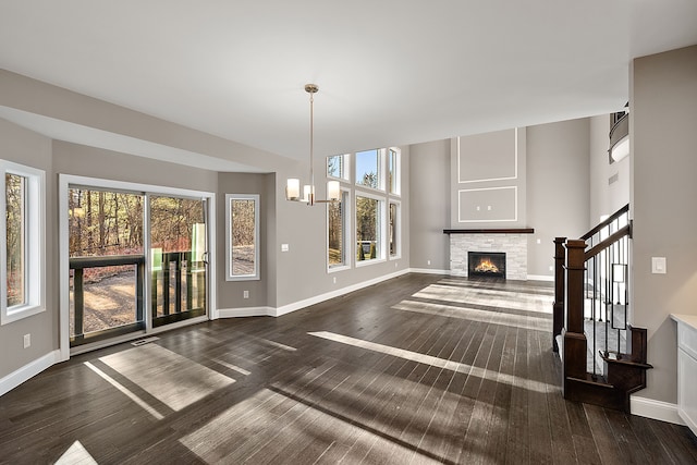 unfurnished living room featuring an inviting chandelier, a stone fireplace, dark wood-type flooring, and a healthy amount of sunlight