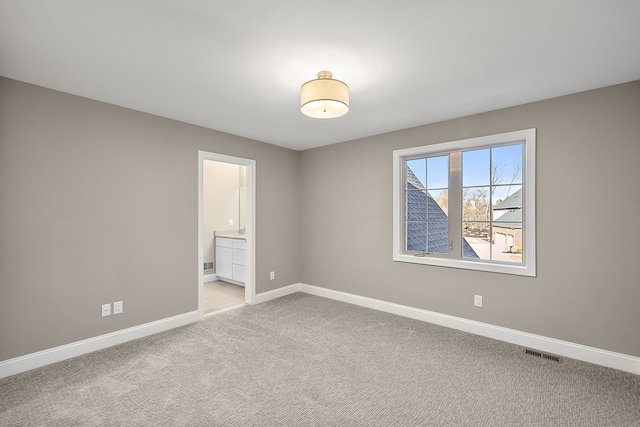 unfurnished bedroom featuring baseboards, ensuite bath, visible vents, and light carpet