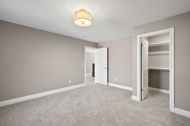 unfurnished bedroom featuring a spacious closet, a closet, light carpet, and baseboards