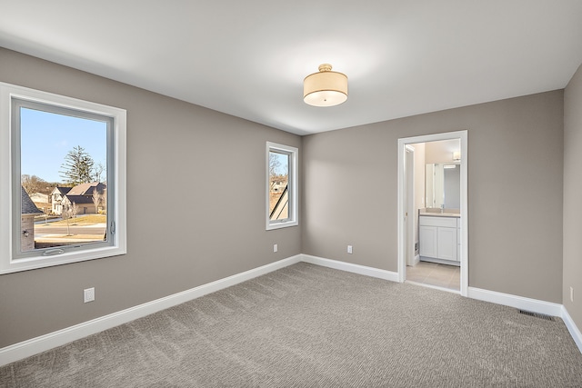 unfurnished bedroom with light carpet, baseboards, and connected bathroom