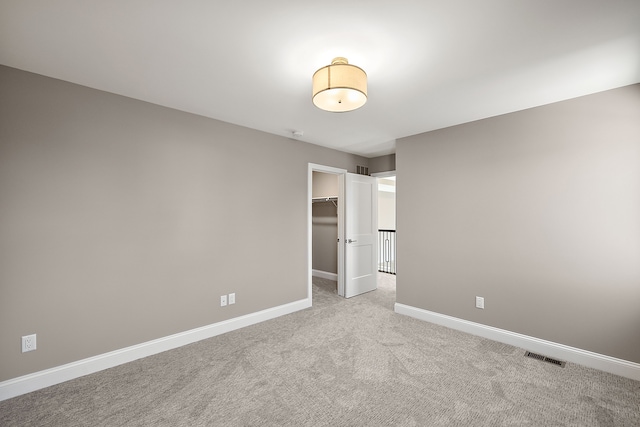 unfurnished bedroom featuring light colored carpet, a closet, a walk in closet, baseboards, and visible vents
