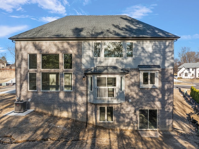 rear view of property featuring roof with shingles, brick siding, and central AC