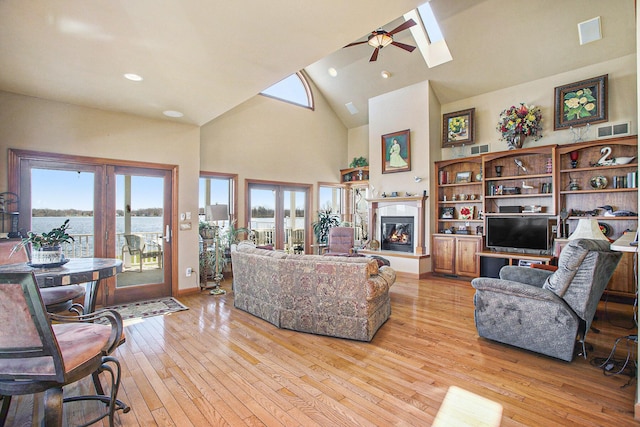 living area featuring french doors, high vaulted ceiling, a skylight, light wood-style floors, and ceiling fan