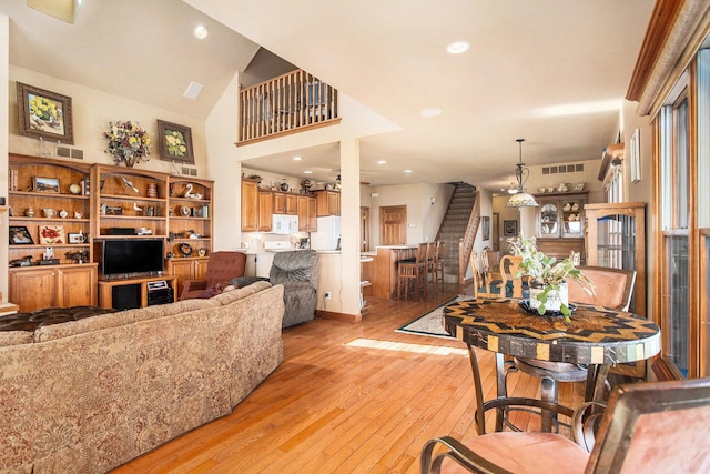 dining room featuring light wood-type flooring, a towering ceiling, stairway, and visible vents