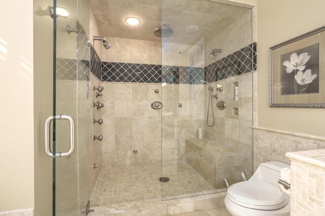 full bathroom featuring tile walls, toilet, a shower stall, and wainscoting